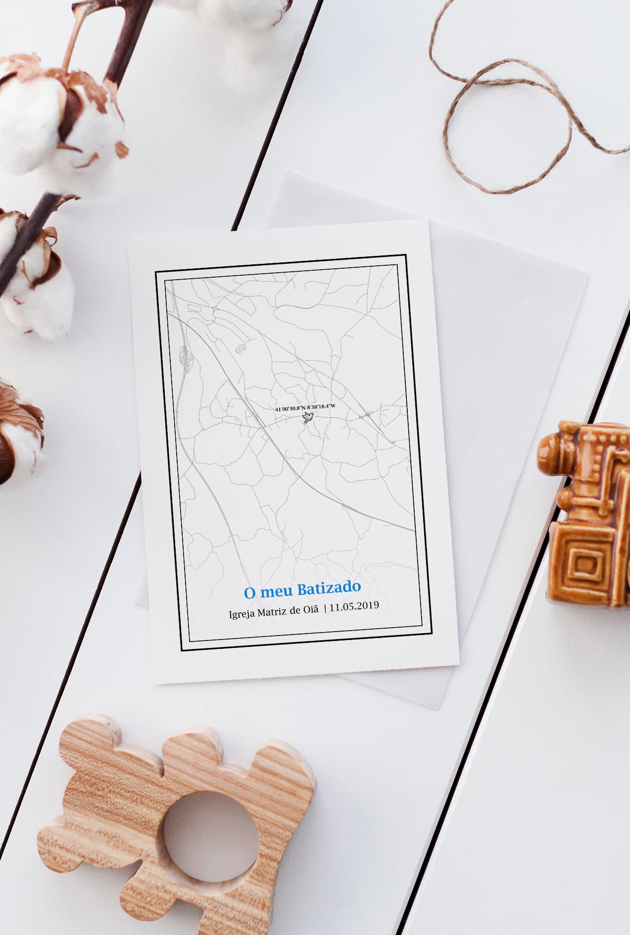 Convite de batizado com mapa e texto em papel branco sobre mesa branca com decoração